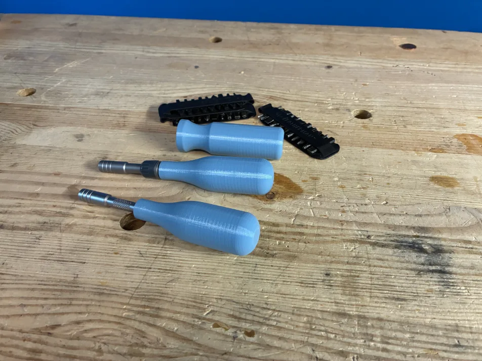 A blue 3D printed screwdriver handle surrounded by screwdriver bits